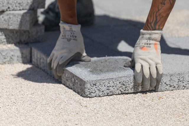 Hands positioning a paving stone on its laying bed