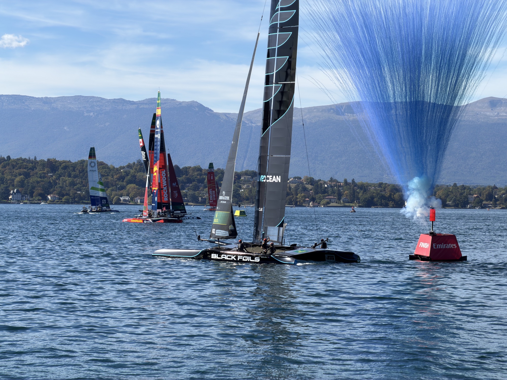 The Black Foils catamaran near the finish line with blue smoke